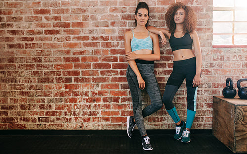 Two young women standing by wall in gym