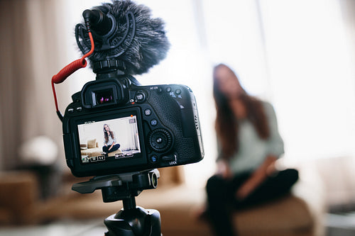 Young woman recording video for her vlog using camera with microphone mounted on tripod.
