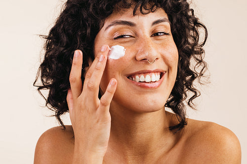 Attractive young woman applying moisturizing cream on her face