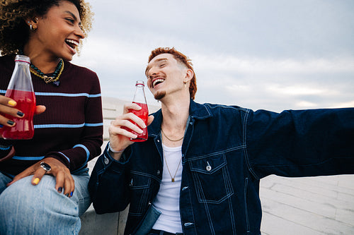 Friends laughing and drinking soda together outdoors