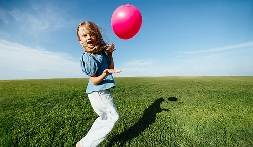Girl throws pink ball in the air on open field