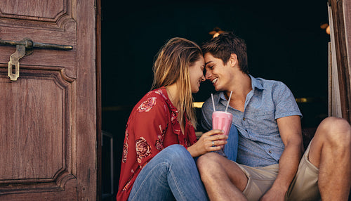 Happy couple sitting outdoors holding a milkshake