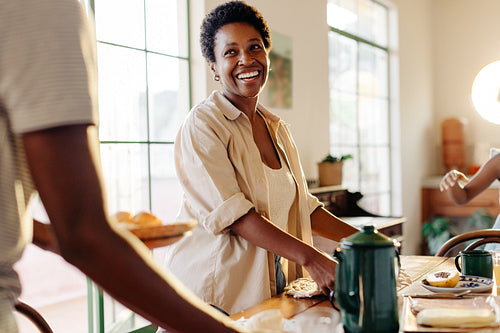 Mother preparing the breakfast table with her son, serving Brazilian cheese bread rolls