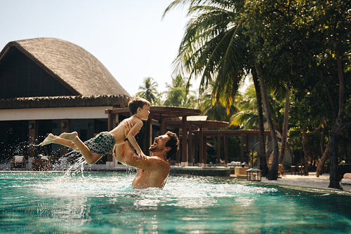 Father playing with child in island resort swimming pool
