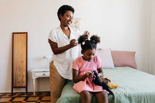 Happy mother dressing her daughter's afro hair in the bedroom