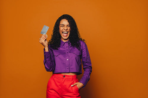 Excited woman smiling while paying with contactless card on vibrant orange background