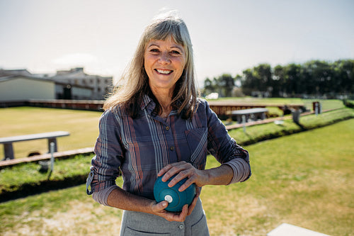 Elderly woman standing in a lawn holding a boule