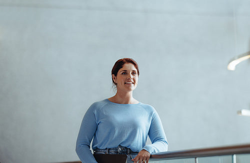 Business woman with ginger hair stands on an interior balcony in a modern office