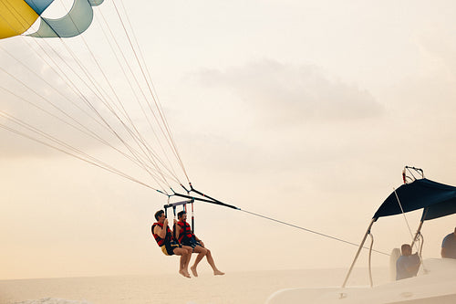 Two men parasailing from a motorboat over the ocean at sunset