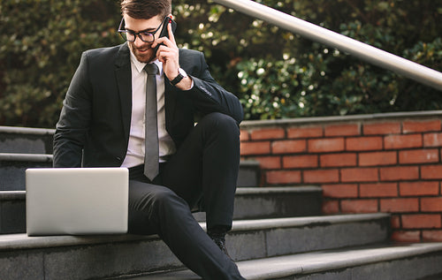 Businessman on steps with phone and laptop