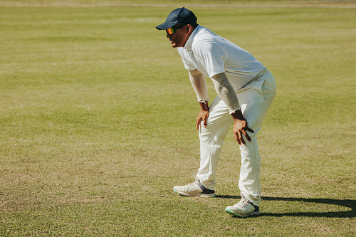 Fielder crouched on cricket field during daytime in athletic stance
