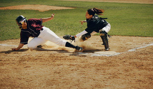 Base runner slides safely into home plate as the catcher attempts a tag during a competitive baseball game