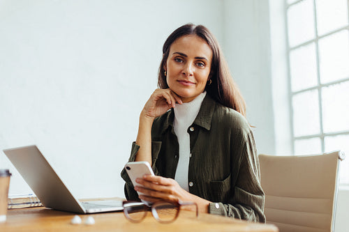 Business woman sitting in an office with a smartphone in her hand