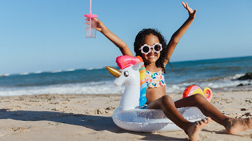 Happy girl having fun at the beach with a unicorn floaty