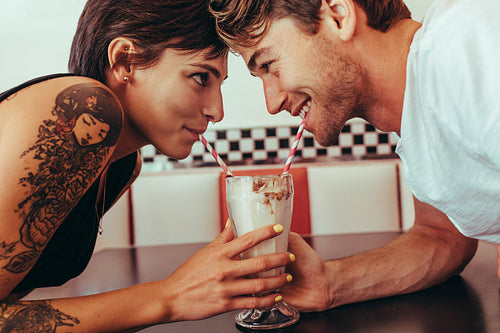 Romantic couple sharing milk shake using straws from the same glass