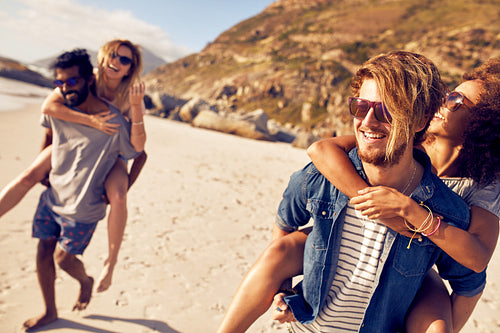 Young men piggybacking women on the sea shore