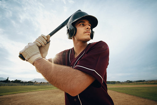 Baseball batter ready to swing at pitch with gloves on picturesque field under summer sky
