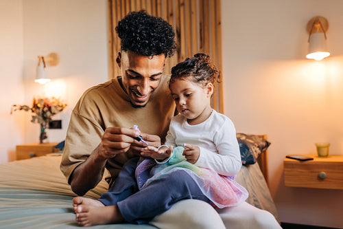 Smiling single dad painting his daughter's nails with nail polish