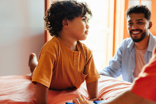 Young boy relaxing on a bed with a smiling adult nearby