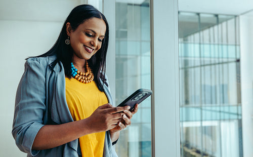Indian businesswoman smiling while using her smartphone in a modern office environment
