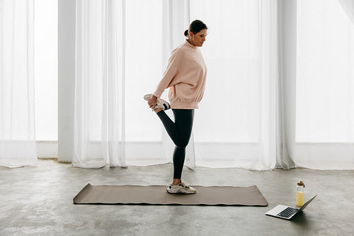 Woman following a home stretching workout with yoga guidance on a laptop