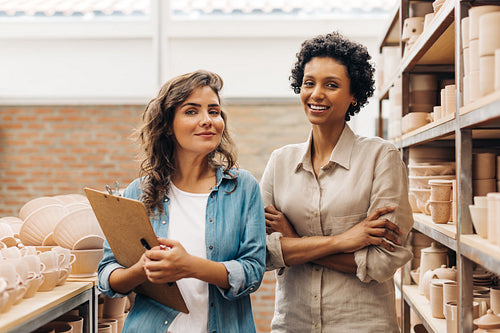 Successful female ceramists smiling at the camera in their store