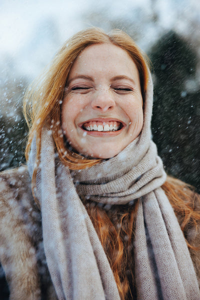 Woman enjoys a knitted scarf beneath falling snow