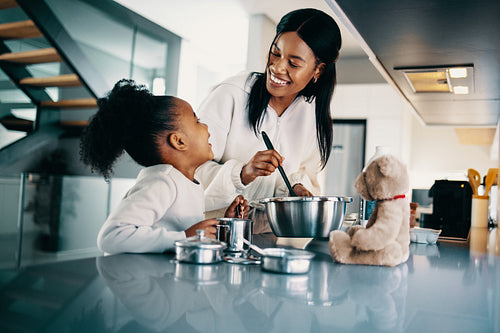 Little girl helping her mother with making food in the kitchen