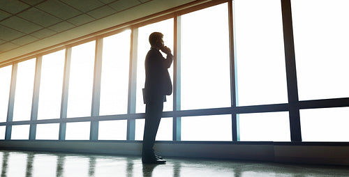 Businessman standing near office window and talking on mobile phone