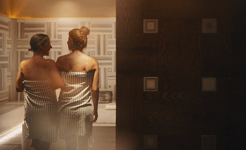 Mature woman and young woman entering a luxury hammam spa together, wrapped in towels, sharing a moment of relaxation and bonding