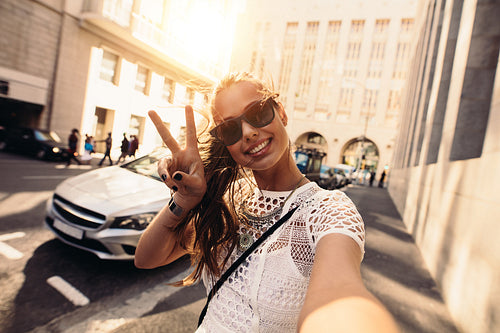 Young woman taking selfie in a street surrounded by buildings.