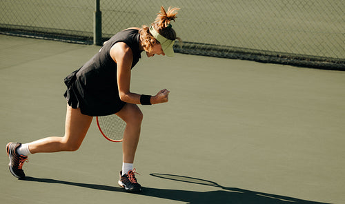 Sporty blonde woman celebrating with a fist pump on an outdoor tennis court