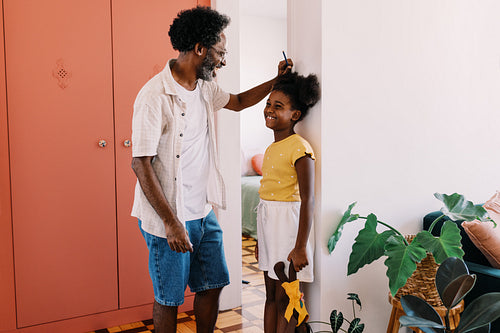 Mature dad measuring his daughter's height against a wall at home