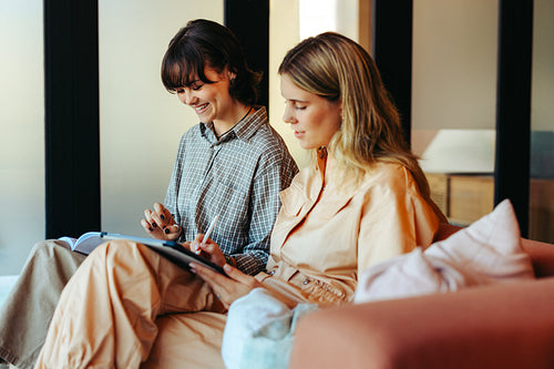 Friends studying together with digital tablet and book in modern cozy living room setting