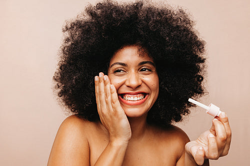 Woman with Afro hair applying cosmetic oil on her face