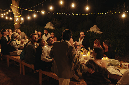Outdoor dinner party with friends enjoying speech under string lights