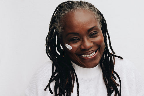 Happy mature woman applying beauty cream on her face