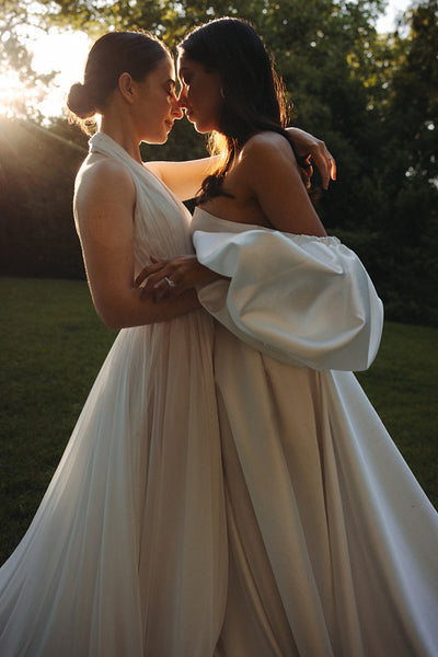 Two brides embracing in a sunlight garden setting