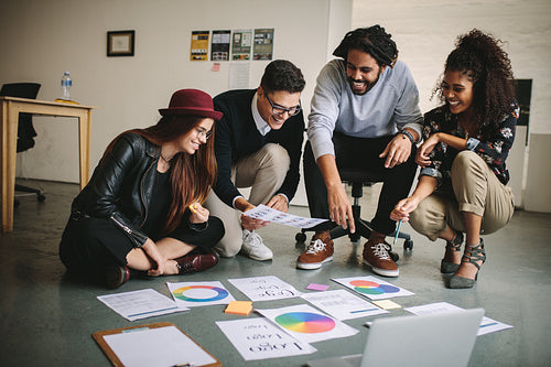 Business people discussing plans sitting on floor with papers and laptop