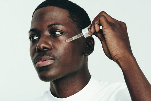 Young black man moisturizing his skin with a facial oil in a studio