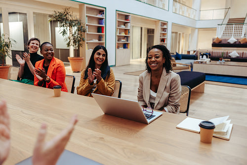 Diverse colleagues clapping for an African-American female colleague during a business meeting