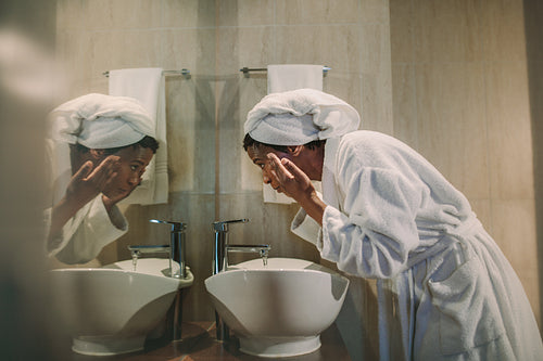 African woman washing her face in bathroom sink