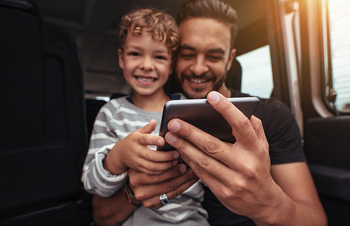 Happy father and son at the back of car with digital tablet
