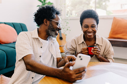 Husband showing wife smartphone screen, relaxing in living room