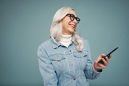 Cheerful grey-haired woman holding a amsrtphone in a studio