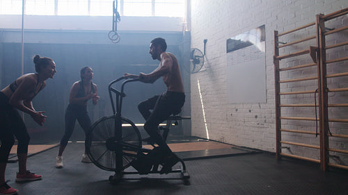 Man exercising on air bike in gym with friends