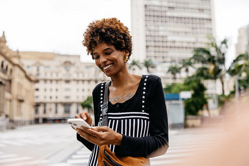 Stylish woman using smartphone in urban setting with buildings