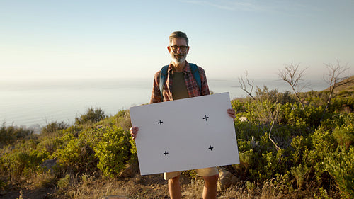 Senior hiker with blank poster on a mountain hike