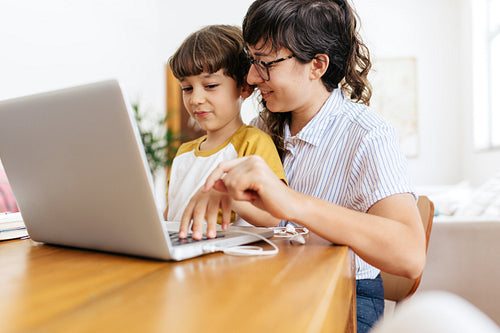 Woman teaching son how to use a laptop at home