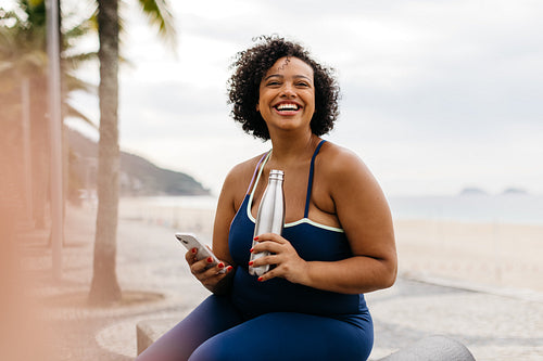 Fitness woman takes a refreshing break with her smartphone on beach promenade